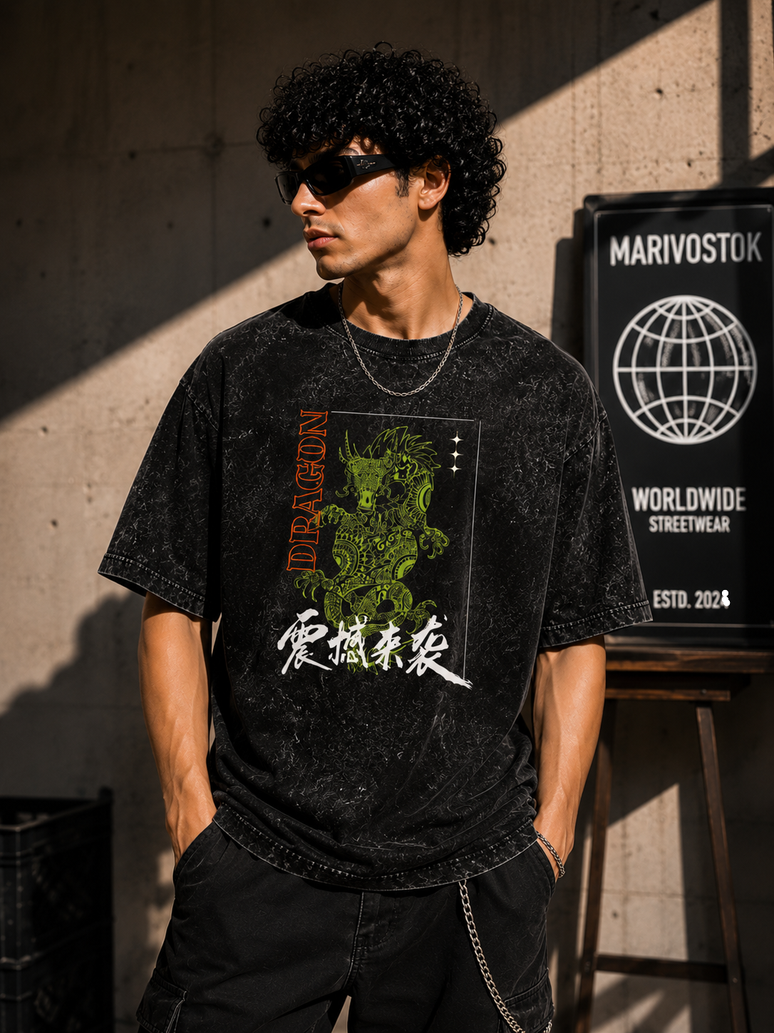 Person wearing a black t-shirt with a graphic design, standing against a wall with a sign in the background.