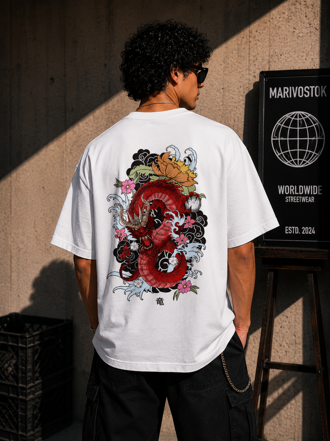 Person wearing a white t-shirt with a colorful dragon design on the back, standing against a textured wall.